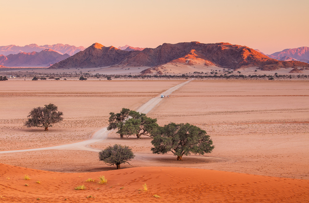 Blick von der Elim Düne Richtung Sesriem Camp zu Sonnenuntergang. Im Hintergrund leuchten die Naukluvt-Berge.